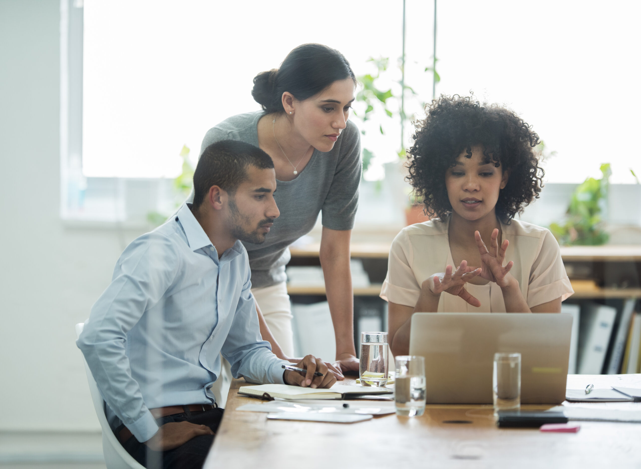 A group of accounting professionals gather around a laptop, discussing how to help clients build cash reserves.